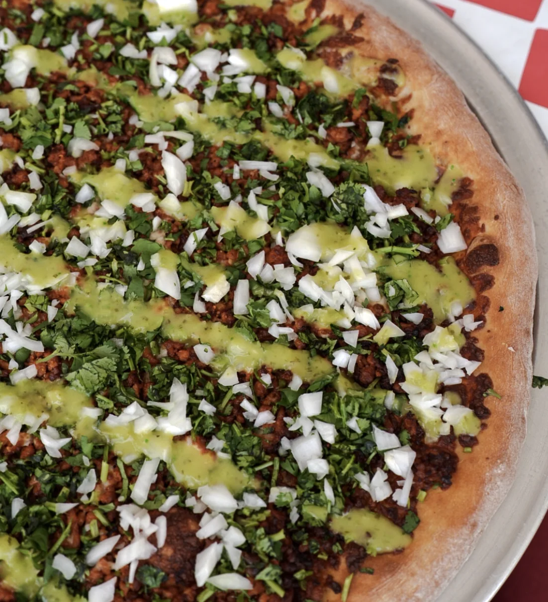Specialty pizza topped with seasoned meat, cilantro, onion, and green sauce